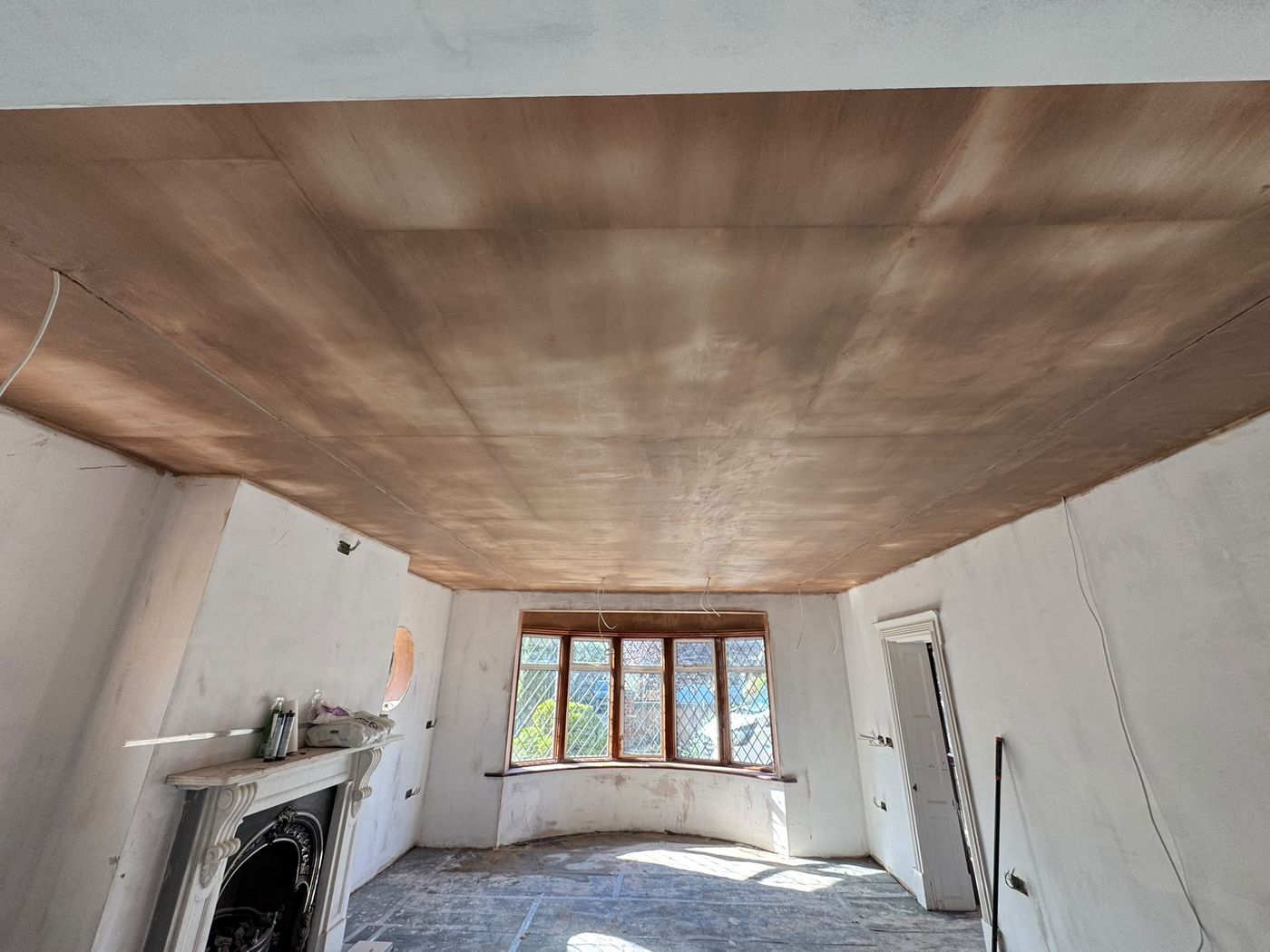 A freshly plastered living room with a bay window and fireplace